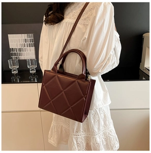 Détail du sac cabas matelassé bordeaux avec garniture dorée porté sur robe blanche