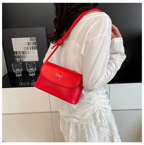 Chic red shoulder bag with silver bow accent and knotted strap on white dress