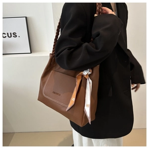 Detail of a brown leather tote bag with woven handles and a floral scarf decoration