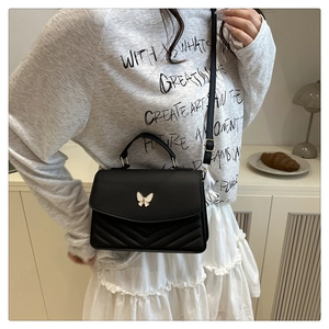 Detail of black crossbody bag with gold butterfly badge and V-shape quilted stitching