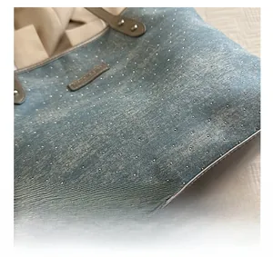 Detail of light blue denim tote bag with silver rhinestones and grey leather handle