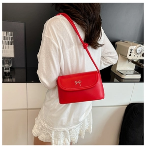 Detail of red leather crossbody bag with silver bow accent and knotted shoulder strap
