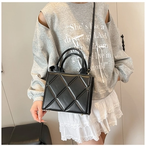 Détail d'un sac cabas matelassé noir avec pieds dorés et doubles anses sur modèle
