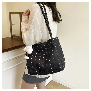 Detail of black quilted tote bag with white bow prints and a soft cloud pendant charm