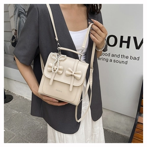 Close-up of cream white backpack featuring 3D bows, pearl pendant, and leather texture