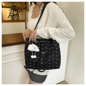 Detail of a black pleated tote bag with white bow prints and a plush cloud charm