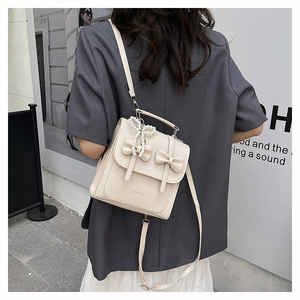 Detail of beige backpack with ribbon bows and pearl tassel worn by a model in city street