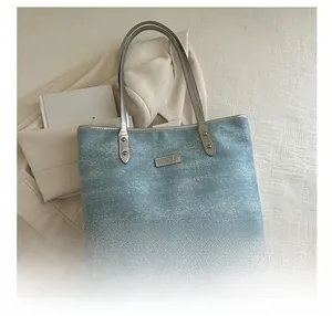 Detail of light blue denim tote bag with rhinestones and silver handles for daily commute