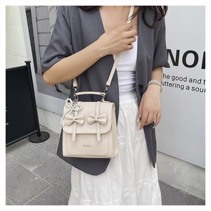 Close-up of cream bow backpack with pearl chain detail and elegant fashion lettering