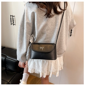 Rear view of a model wearing a black PU leather crossbody bag with silver bow accent