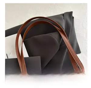 Detail view of smooth brown leather handles and khaki canvas fabric on a tote bag