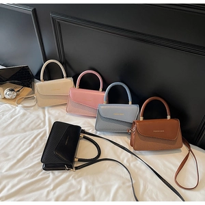 Cinq sacs à bandoulière en cuir élégants aux tons pastels disposés sur un lit blanc