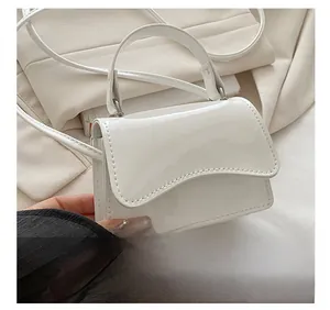 Close-up of white glossy mini handbag with flap closure and fine shoulder strap