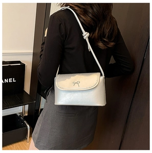 Detail of silver metallic crossbody bag with a decorative metal bow on the front flap