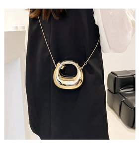 Detail of a decorative gold mini crossbody bag with circular cutout design and chain strap