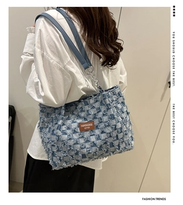 Blue denim tote bag with checkerboard pattern and frayed edges shown on a model