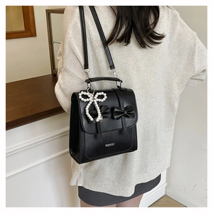 Detail of black faux leather backpack with chic bow accents and pearl pendant