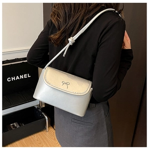 Detail of silver metallic crossbody bag with bow buckle worn on a shoulder strap