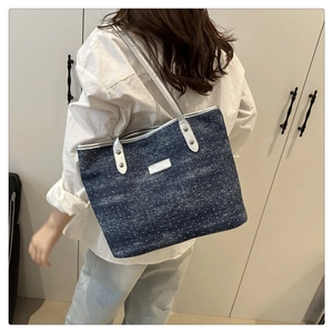 Detail of dark blue polka dot tote bag featuring metallic silver straps and brand plate