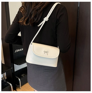 Detail of white square crossbody bag with bow buckle worn by a model in a studio setting