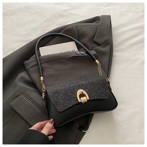 Detail of sequin flap and golden horseshoe buckle on black leather shoulder bag