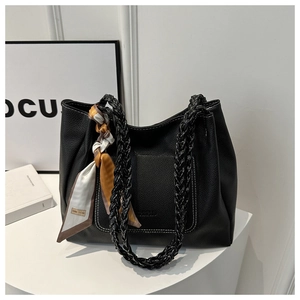 Dettaglio borsa tote in pelle nera con manici intrecciati e foulard in seta stampato