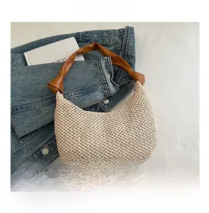 Nahaufnahme der beigen Strohtasche mit geknotetem braunem Ledergriff und Smartphone-Größe