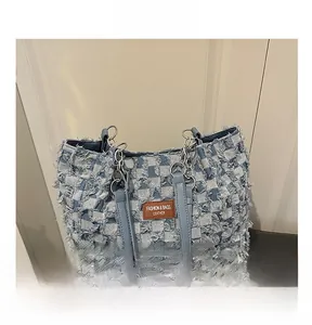 Detail of checkered denim patchwork tote with frayed edges and brown leather logo tag