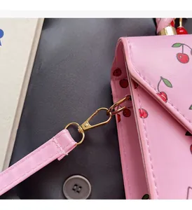 Détail du fermoir en métal doré sur un sac en cuir rose avec imprimé cerise