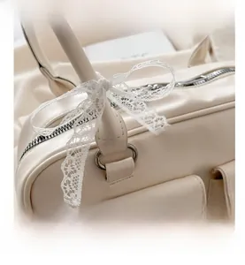 Close-up of off-white multi-pocket pillow bag with decorative lace bow and silver zipper