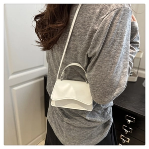 Detail of white glossy mini leather handbag with crossbody strap shown on model
