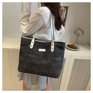 Detail of dark grey polka dot tote bag featuring silver leather handles and brand tag