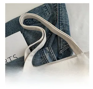 Detailed close-up of thickened canvas handle and stitching on off-white tote bag