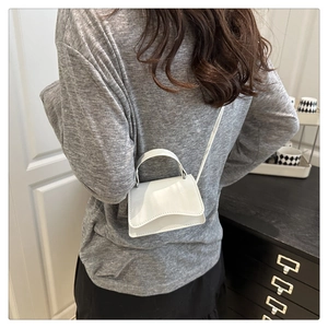 Close-up of a mini white glossy leather crossbody bag worn by a model in a minimal setting
