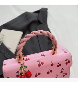 Détail du sac à main rose à cerises avec poignée tressée et pendentif cerise