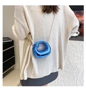 Detail of the bright blue mirrored acrylic crescent bag with a gold chain strap on a model