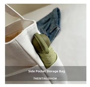 Close-up of white canvas tote bag side pocket holding a green folding umbrella