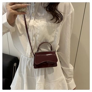 Detail of burgundy patent leather mini crossbody bag with glossy finish and top handle
