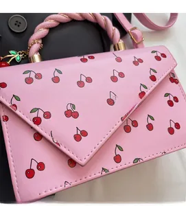Détail d'un sac à main en cuir rose avec imprimé cerise et poignées tissées sur tissu