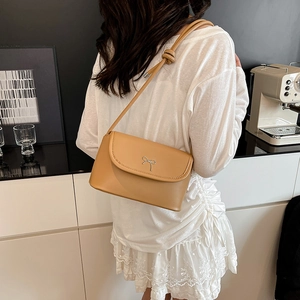 Modern khaki shoulder bag with silver bow buckle and knotted strap shown in a cafe setting