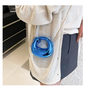 Detail of metallic electric blue crescent bag with fine gold chain strap on model