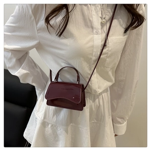 Model wearing a mini dark red patent leather crossbody bag over a white shirt