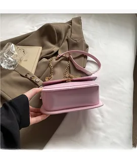 Detail of light pink leather saddle bag with gold chain strap on a brown suit