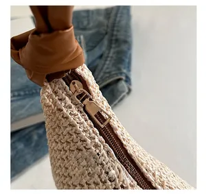 Detail der gewebten Strohtasche mit braunem Lederknotengriff und goldenem Reißverschluss