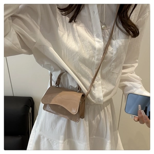 Detail of khaki patent leather handbag with wavy flap and metallic strap attachments