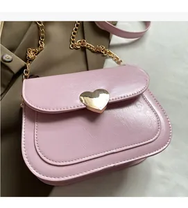 Detail of pink PU leather saddle bag featuring a gold heart clasp and chain strap