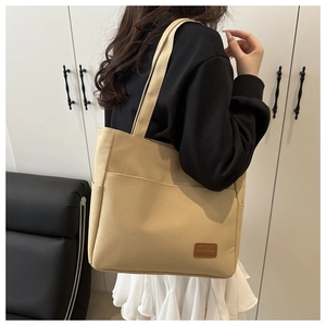 Detail view of beige canvas tote bag with side pockets and brown leather brand patch