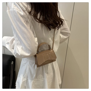 Detail of a mini khaki patent leather bag with a unique wavy bottom and shoulder strap