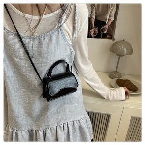 Mini glossy black crossbody bag with wave flap shown on model in a minimalist room