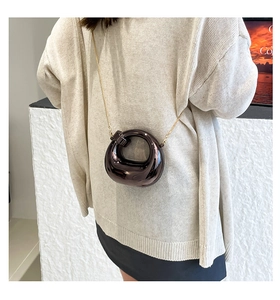 Detail of a dark metallic crescent bag featuring a gold chain and unique sculptural ring design